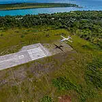 Helipad and small aircraft near lush green coastline.