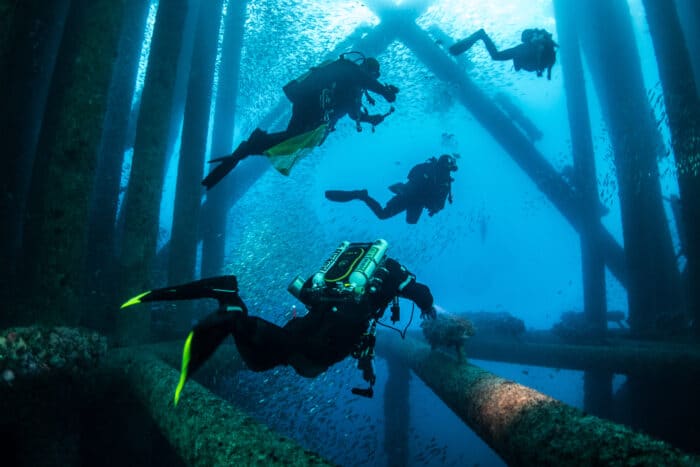 Technical Diving - Scuba Divers with Closed Circuit Rebreathers diving under an oil rig