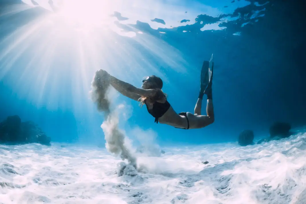 Woman freediver with white sand over sandy sea with fins. Freediving underwater in ocean