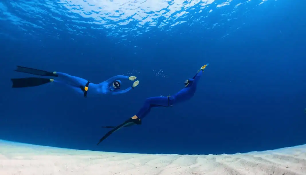 Two freedivers having fun over the sandy sea bottom